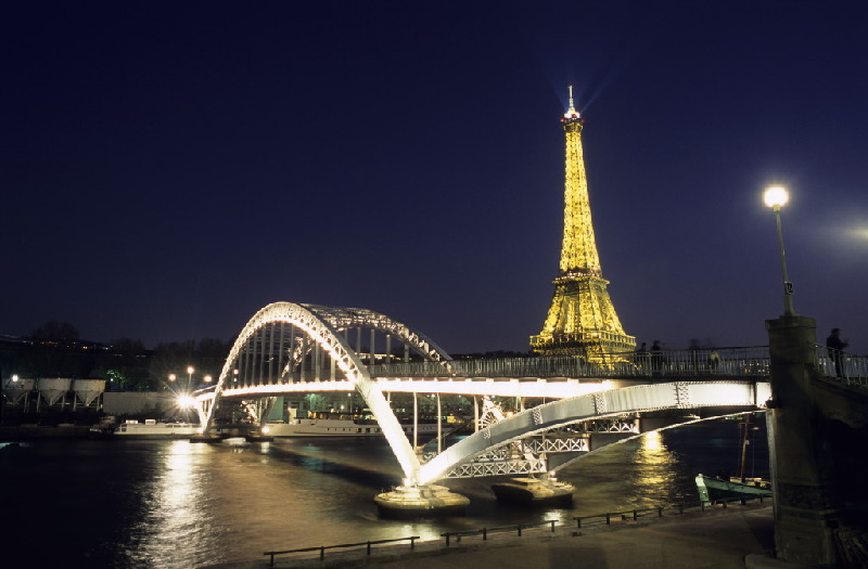 Beleuchteter Eiffelturm, davor die Passerelle Debilly über die Seine. Der als Höhepunkt der Pariser Weltausstellung von 1889 errichtete Eiffelturm.