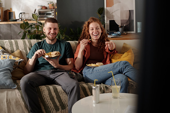 Junge Menschen sitzen lachend auf dem Sofa und gucken einen französischen Film